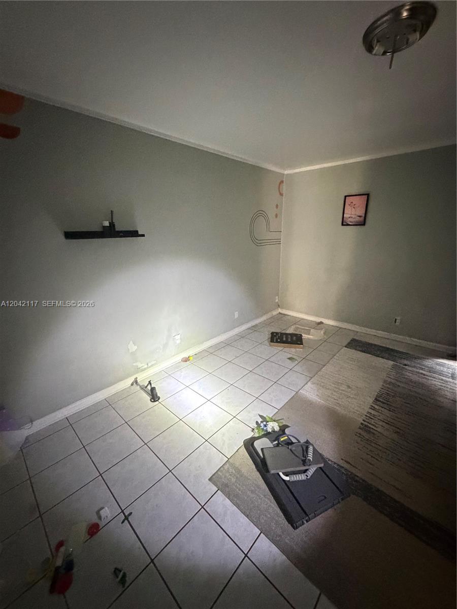 An empty room features gray walls, white tile flooring, a small floating shelf, and a rug — ROYAL PALM BEACH, FL