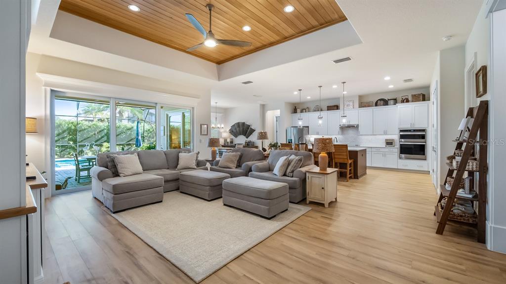 An open-concept living room and kitchen feature a wood-paneled tray ceiling and sliding glass doors — 4008 PINNACLE PLACE COURT, LADY LAKE, FL