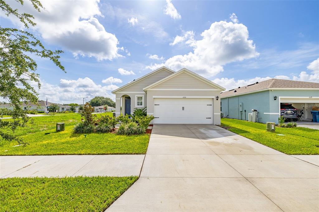 A single-story suburban house with a beige exterior, a two-car garage, and a concrete driveway — 1125 BELFAST PLACE, HAINES CITY, FL