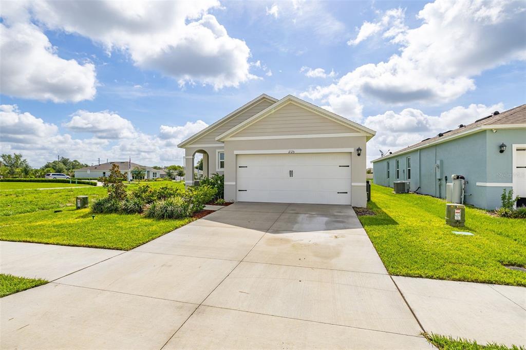 A single-story house with a white garage door and a concrete driveway under a cloudy sky — 1125 BELFAST PLACE, HAINES CITY, FL