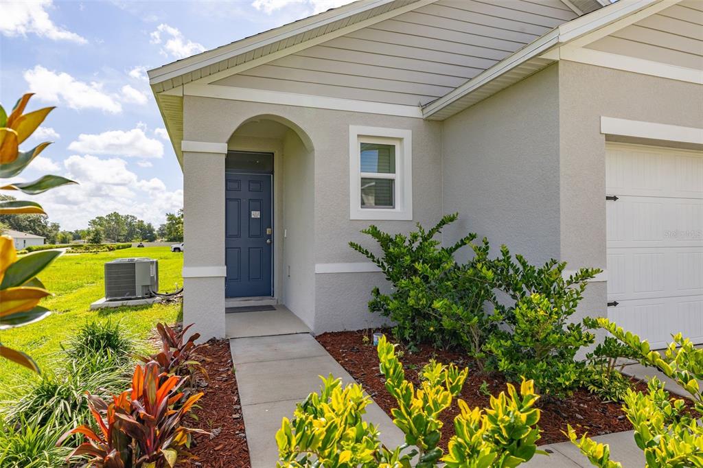 A light gray house exterior features a blue front door, a window, and a garage — 1125 BELFAST PLACE, HAINES CITY, FL