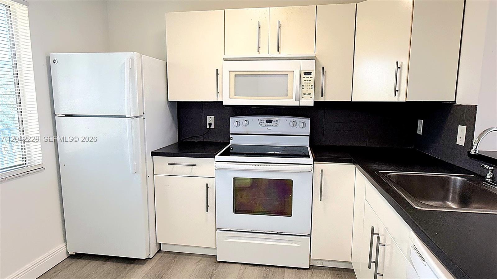 A kitchen features white appliances, white cabinets, and black countertops against a dark backsplash — 8560 N Sherman Cir # 302, Miramar FL 33025, MIRAMAR, FL