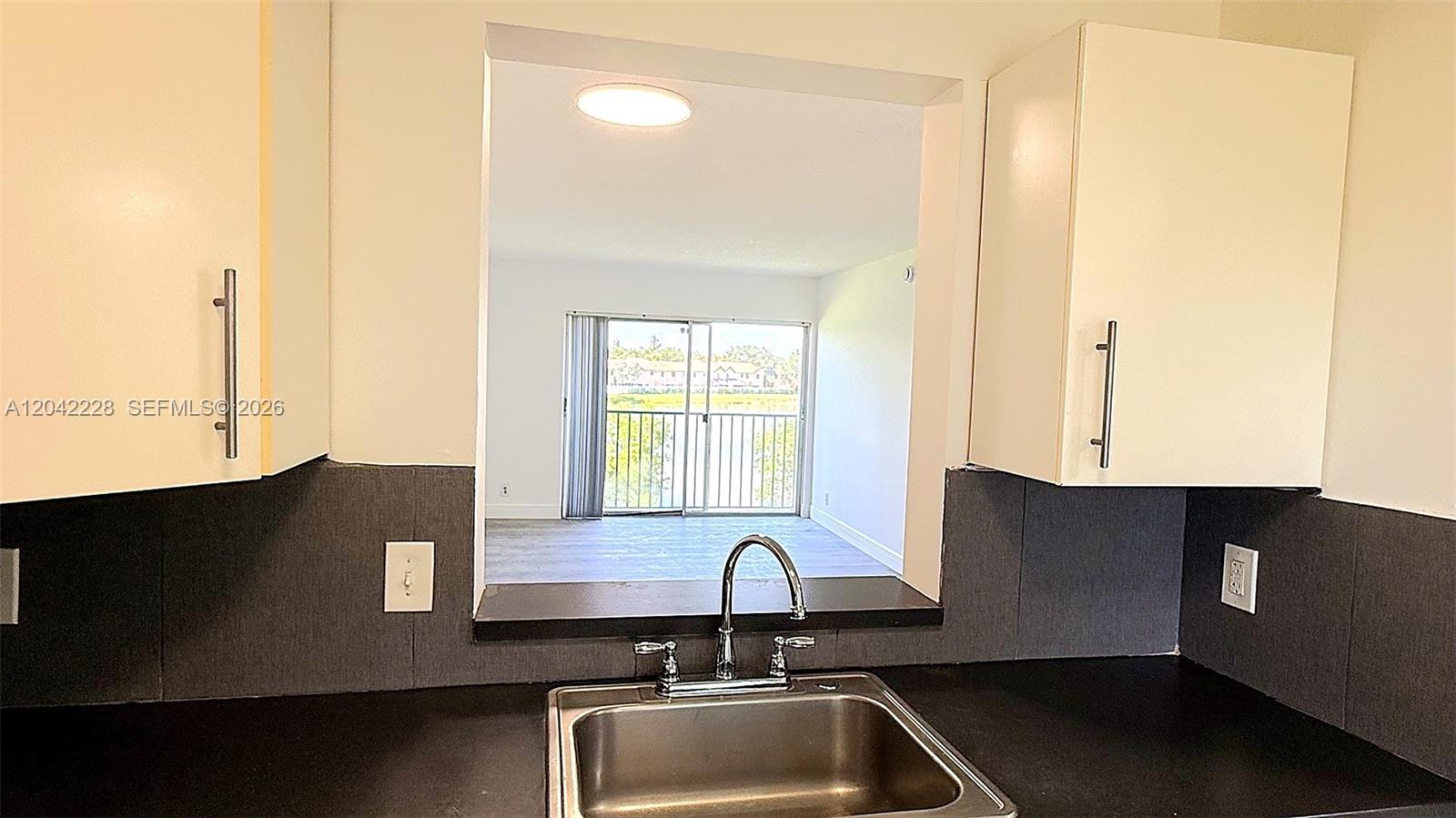 A kitchen sink and counter look through a pass-through window toward a balcony door — 8560 N Sherman Cir # 302, Miramar FL 33025, MIRAMAR, FL
