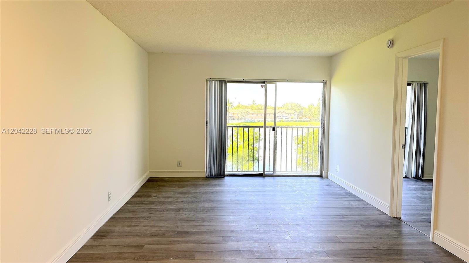 An empty room features wood-look flooring, white walls, and a sliding glass door to a balcony — 8560 N Sherman Cir # 302, Miramar FL 33025, MIRAMAR, FL