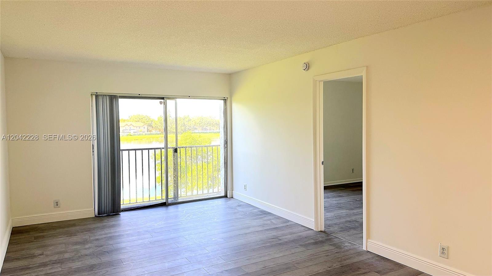 An empty room features wood-look flooring, white walls, and a sliding glass door to a balcony — 8560 N Sherman Cir # 302, Miramar FL 33025, MIRAMAR, FL