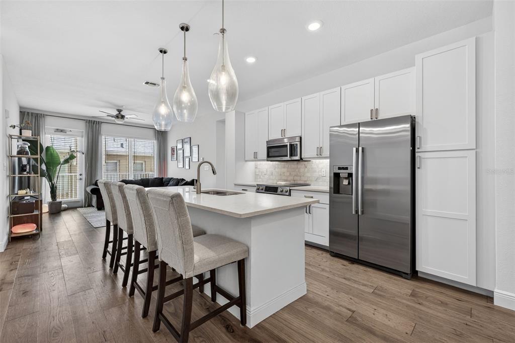 A modern kitchen features white cabinetry, a central island with bar seating, and stainless appliances — 644 3RD AVENUE S UNIT 202, ST PETERSBURG, FL