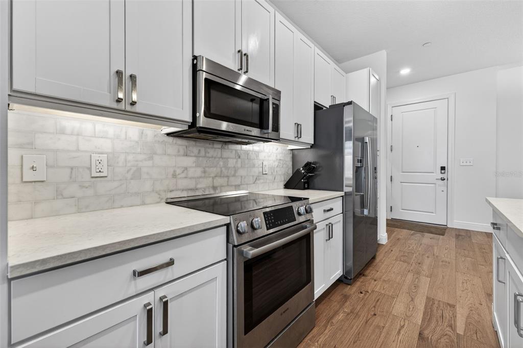 A kitchen features white cabinets, stainless steel appliances, a marble backsplash, and wood-look flooring — 644 3RD AVENUE S UNIT 202, ST PETERSBURG, FL
