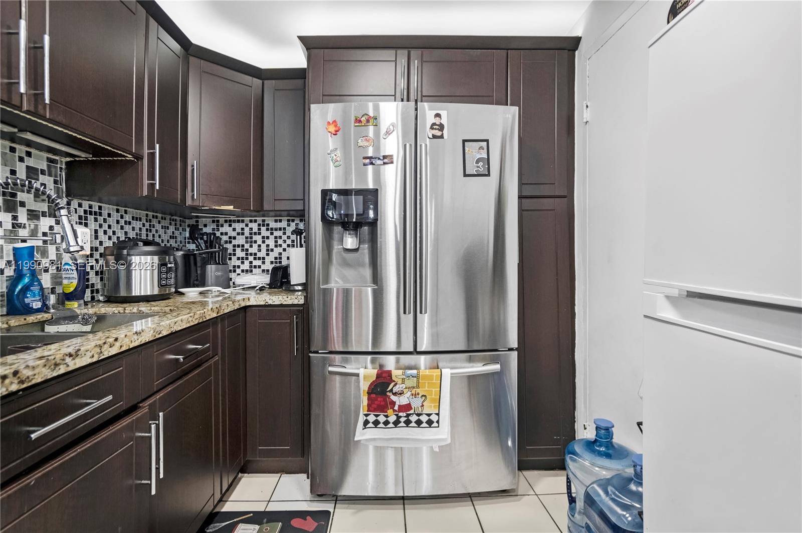 A kitchen features dark wood cabinets, granite countertops, a stainless steel refrigerator, and tiled backsplash — 9403 SW 76th St # Y17, Miami FL 33173, MIAMI, FL