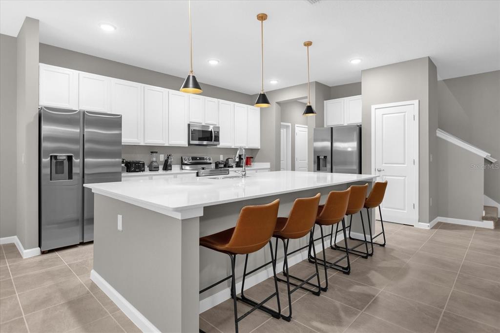 A modern kitchen features white cabinets, stainless steel appliances, a large island, and bar stools — 2441 SHANTI DRIVE, KISSIMMEE, FL