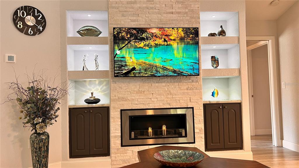 A living room features a stone fireplace, a mounted television, and built-in display shelving — 5556 LEGEND HILLS LANE, SPRING HILL, FL