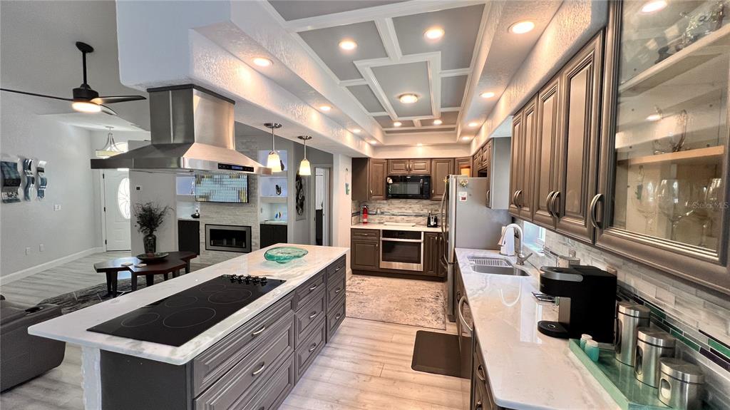 A modern kitchen features a large island with a cooktop, gray cabinetry, and recessed lighting — 5556 LEGEND HILLS LANE, SPRING HILL, FL