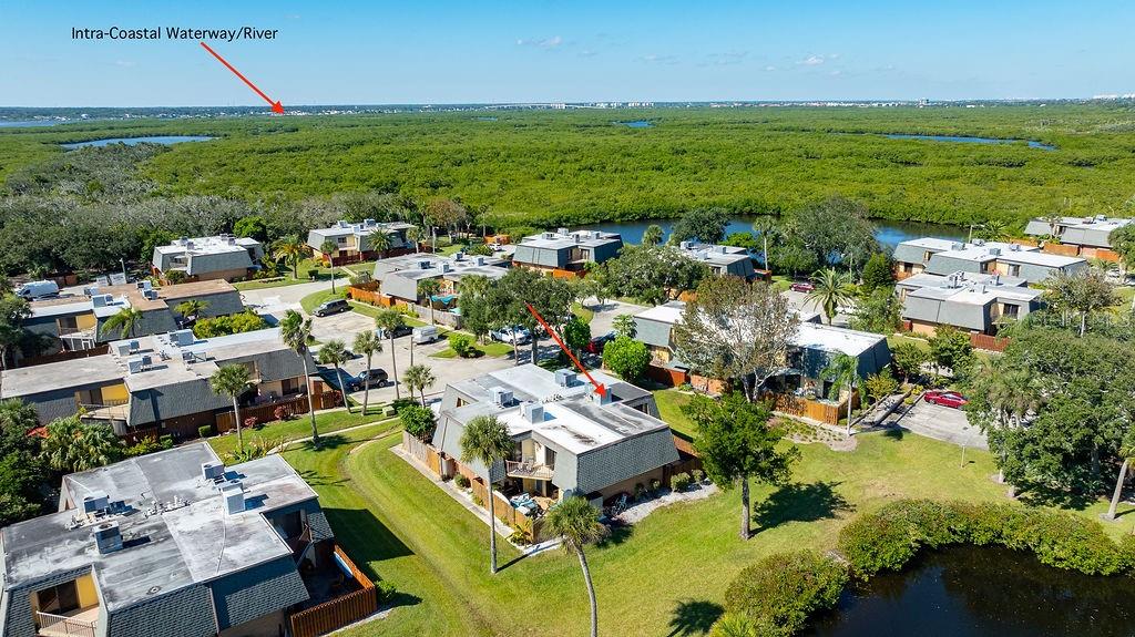 An aerial view shows multiple multi-story residential buildings surrounded by green space and a pond — 113 CEDAR DUNES DRIVE, NEW SMYRNA BEACH, FL