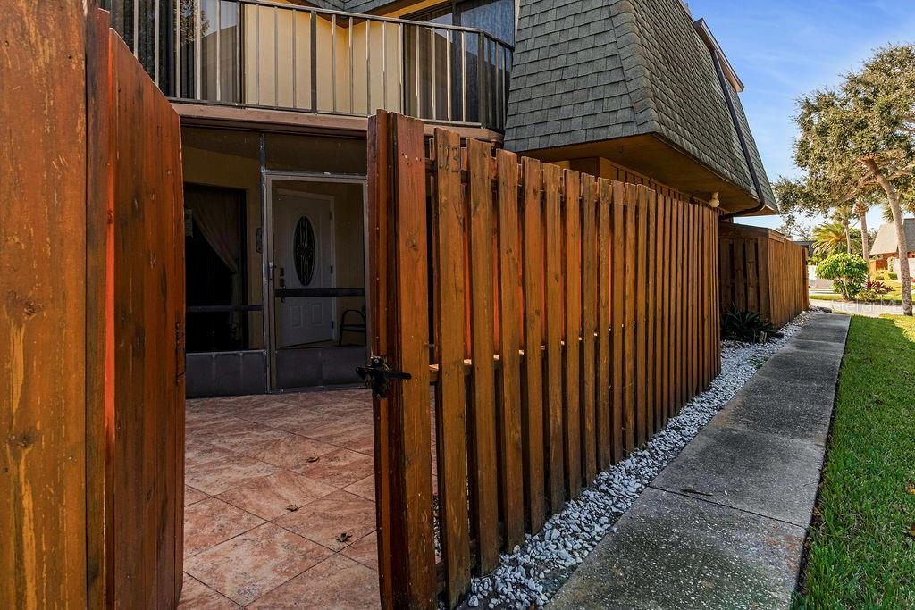 A wooden fence gate opens to a tiled patio area with a screened entry door — 113 CEDAR DUNES DRIVE, NEW SMYRNA BEACH, FL