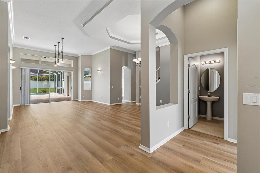 An open-concept living area with light wood flooring, arched doorways, and an adjacent half bathroom — 3102 WHITE PHEASANT PLACE, VALRICO, FL
