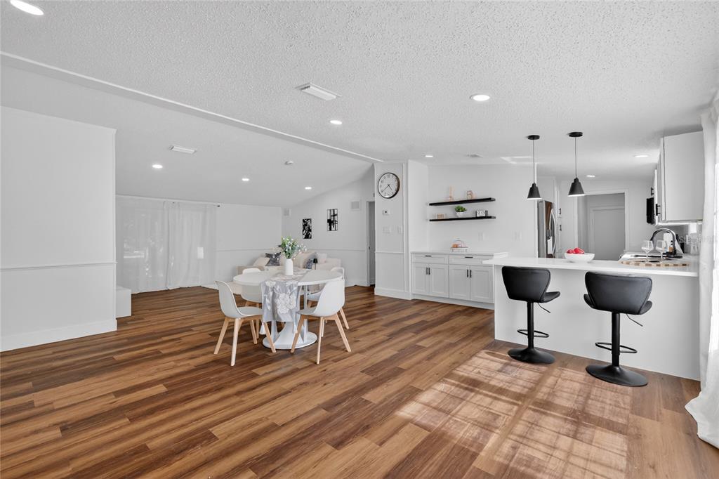 A white kitchen features a breakfast bar with two black stools and wood flooring — 3181 COUNTY ROAD 521B, WILDWOOD, FL