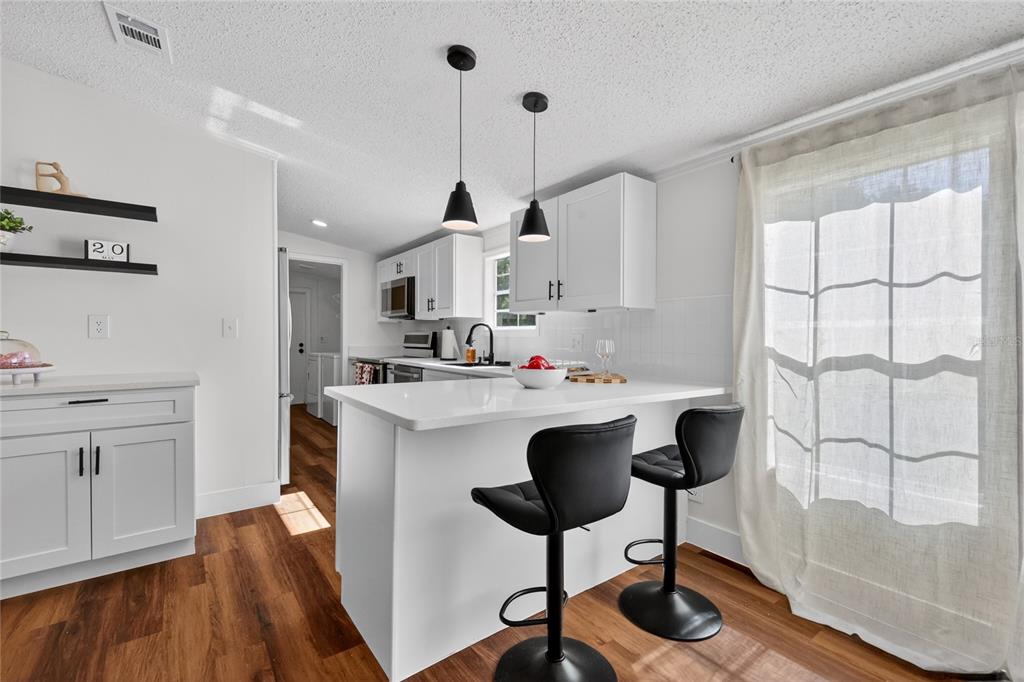 A kitchen with white cabinets, stainless steel appliances, a black faucet, and wood-look flooring — 3181 COUNTY ROAD 521B, WILDWOOD, FL
