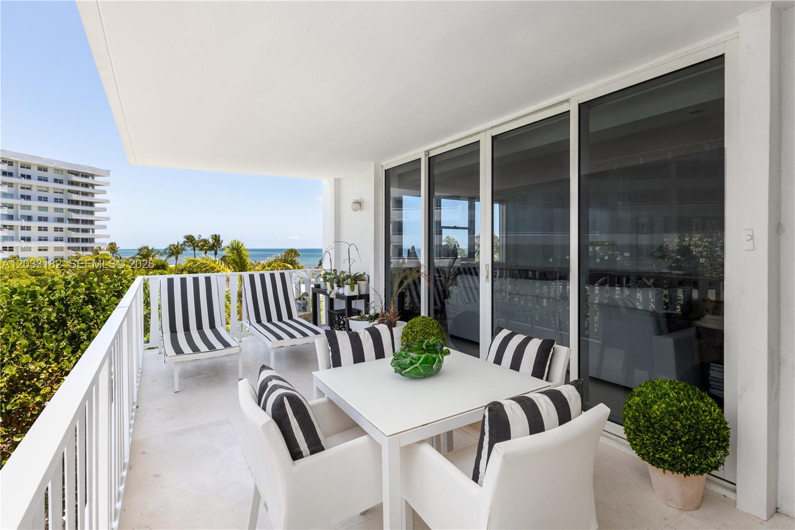 A balcony features a dining set, lounge chairs, and ocean views through a glass railing — 200 Ocean Lane Drive # 409, Key Biscayne FL 33149, KEY BISCAYNE, FL