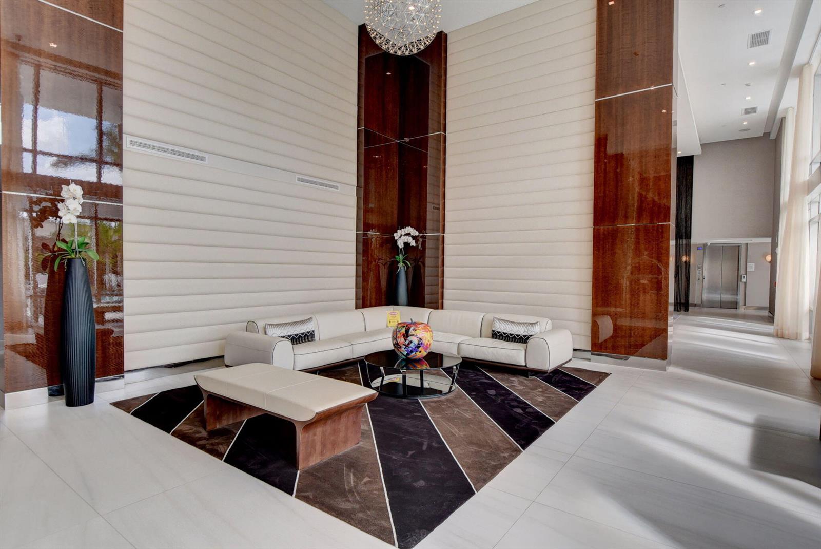 A modern lobby features a white sectional sofa, a patterned rug, and tall wood paneling — 155 E Boca Raton Road, Boca Raton FL 33432, BOCA RATON, FL