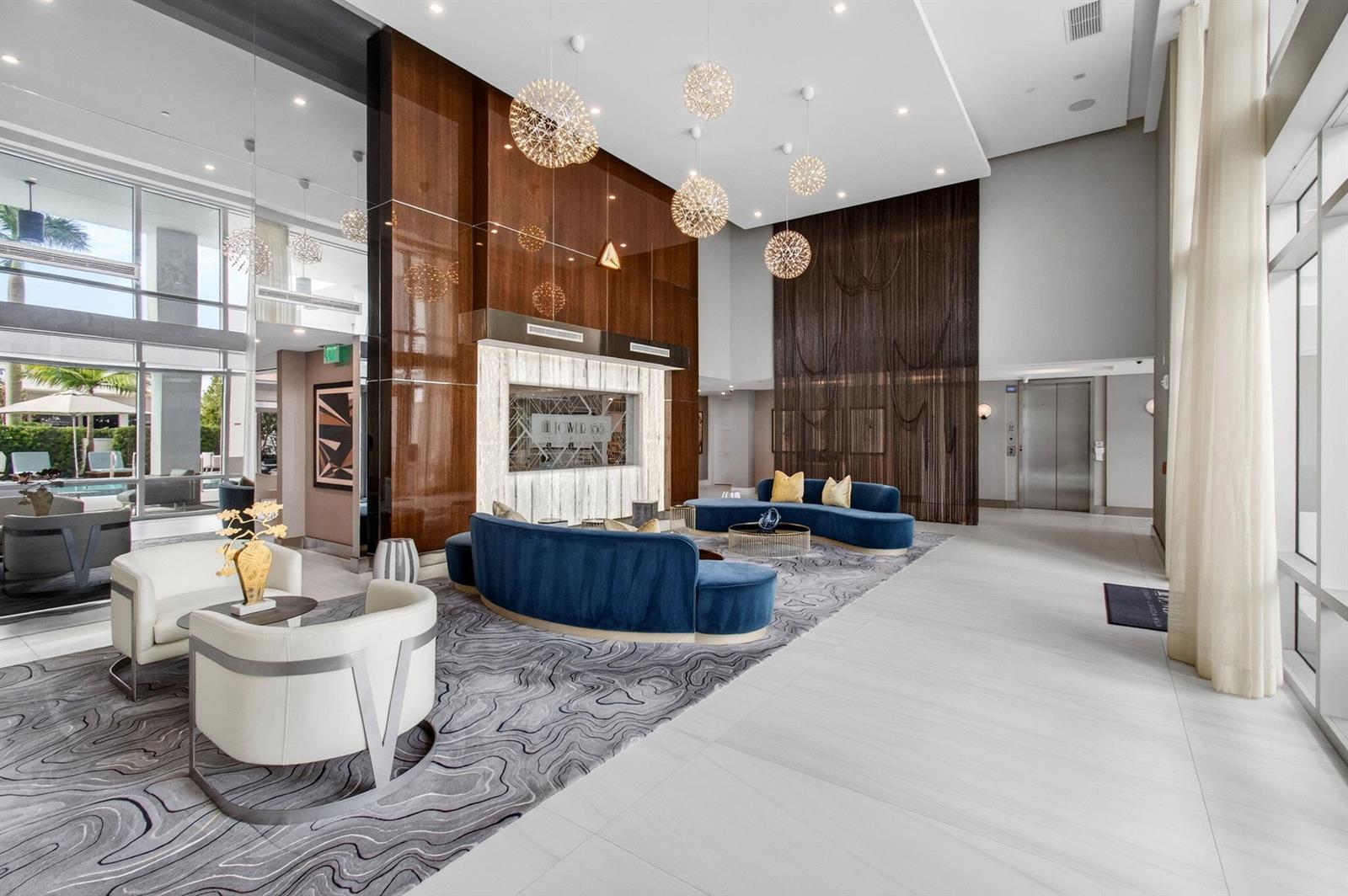 A modern building lobby features blue curved sofas, white armchairs, and decorative pendant lights — 155 E Boca Raton Road, Boca Raton FL 33432, BOCA RATON, FL