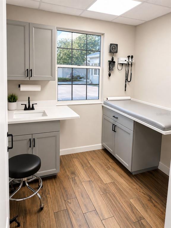 A medical examination room features gray cabinetry, a sink, a treatment table, and wood-look flooring — 2506 ACORN STREET UNIT A-B, FORT PIERCE, FL