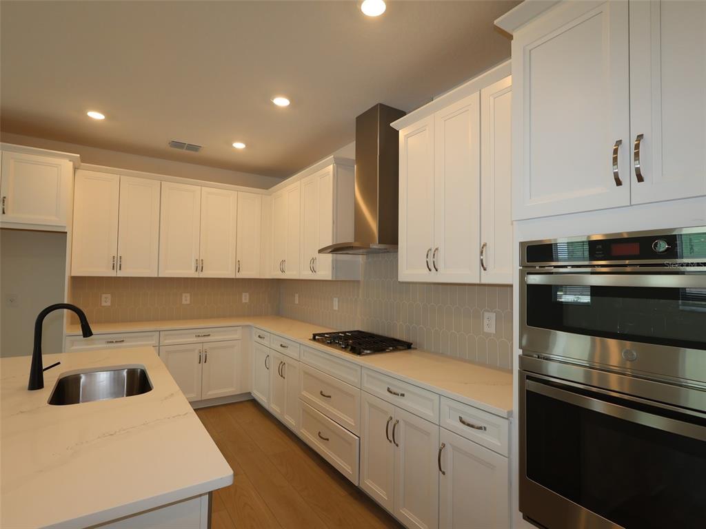 A modern kitchen features white cabinetry, stainless steel appliances, a gas cooktop, and quartz countertops — 4438 SUNSET GARDEN STREET, BRADENTON, FL