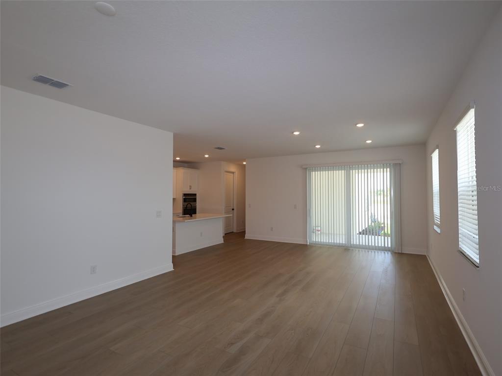 An open-concept living area features light wood-look flooring, recessed lighting, and a sliding glass door — 4438 SUNSET GARDEN STREET, BRADENTON, FL