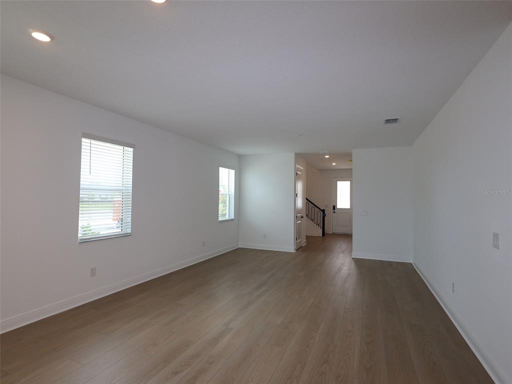 An empty room features light wood-look flooring, white walls, recessed lighting, and two windows — 4438 SUNSET GARDEN STREET, BRADENTON, FL