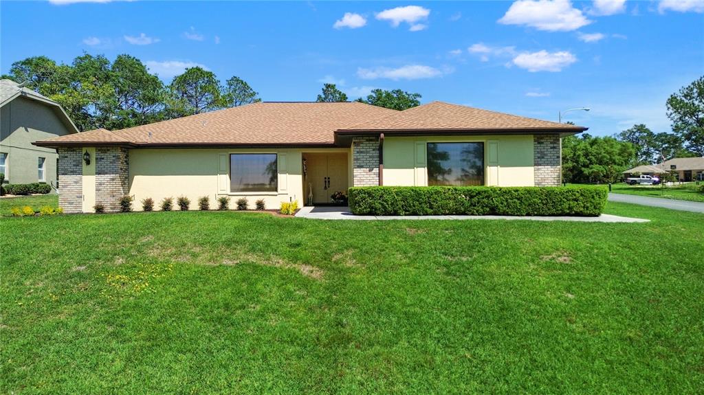 A single-story house with a tan stucco exterior, brick accents, and a large front lawn — 12001 GRANADA PLACE, WEEKI WACHEE, FL
