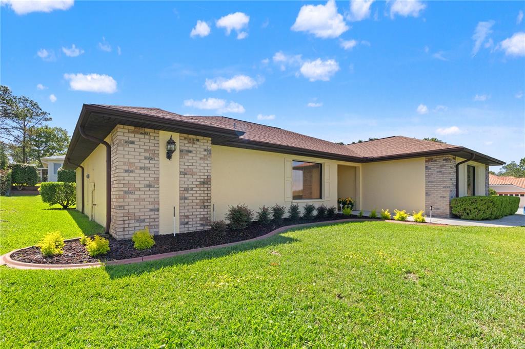 A single-story house with a tan stucco exterior, brick accents, and a brown shingled roof — 12001 GRANADA PLACE, WEEKI WACHEE, FL