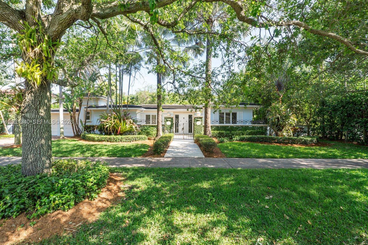 A single-story house with a white exterior is set behind a gated walkway and trees — 1037 Alfonso Ave, Coral Gables FL 33146, CORAL GABLES, FL