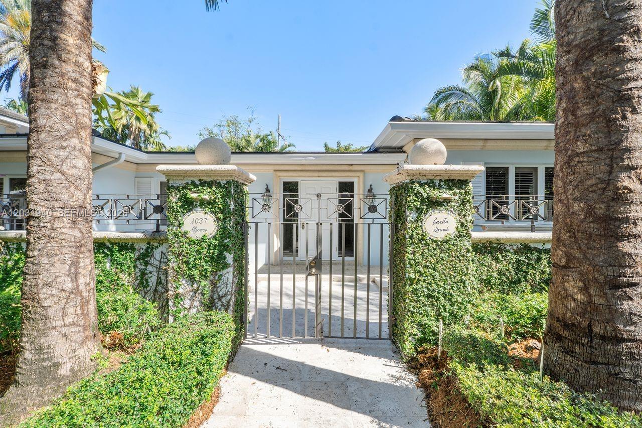 A gated entrance leads to a light blue house with ivy-covered stone pillars — 1037 Alfonso Ave, Coral Gables FL 33146, CORAL GABLES, FL
