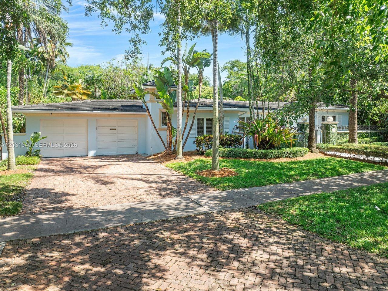 A light blue single-story house features a brick driveway and lush tropical landscaping — 1037 Alfonso Ave, Coral Gables FL 33146, CORAL GABLES, FL