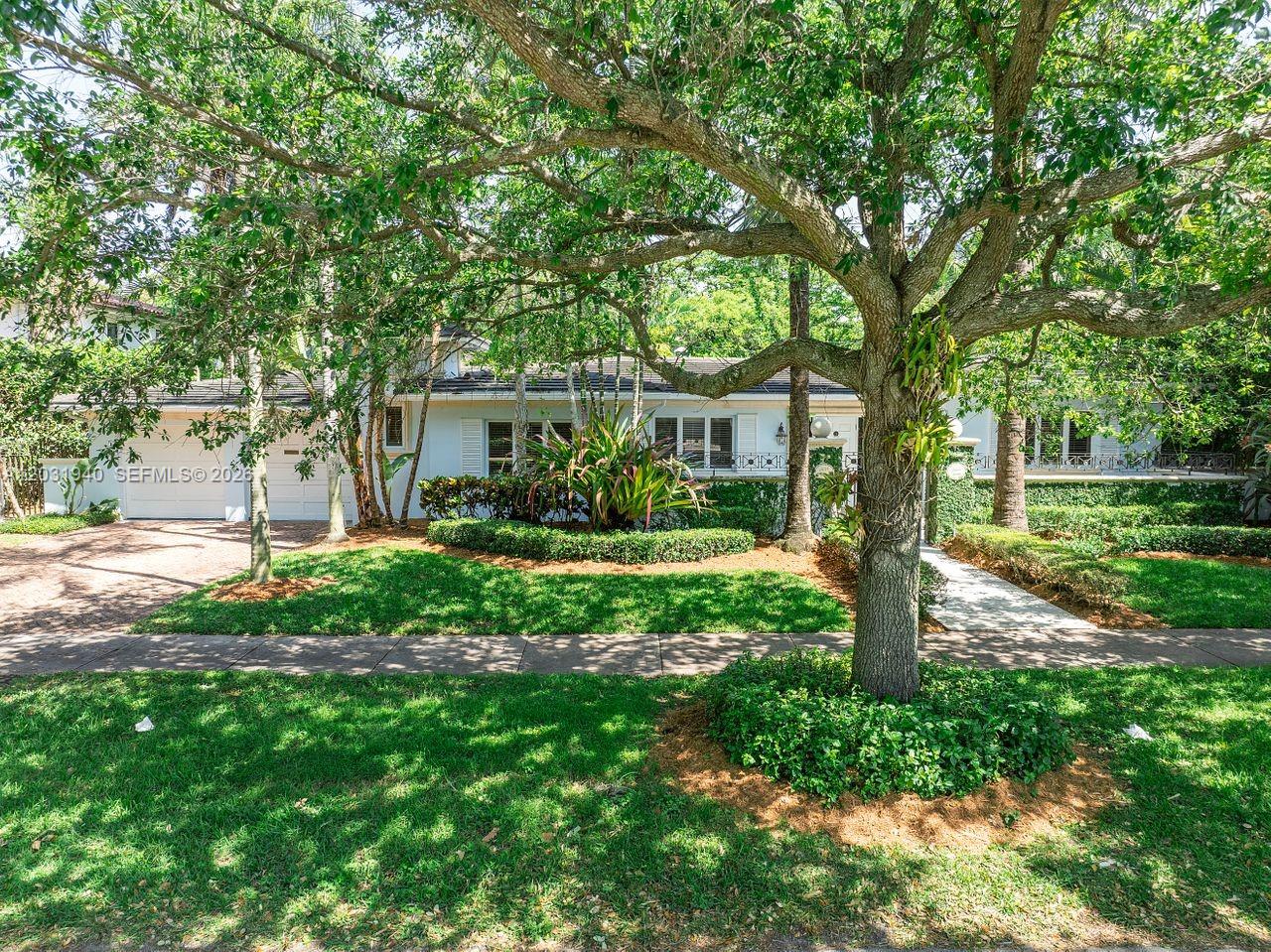 A single-story white house with a paved driveway is partially obscured by large trees — 1037 Alfonso Ave, Coral Gables FL 33146, CORAL GABLES, FL