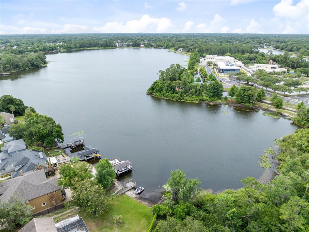 An aerial view shows a lake with residential docks, a boat, and nearby commercial buildings — 5340 N LAKE BURKETT LANE, WINTER PARK, FL