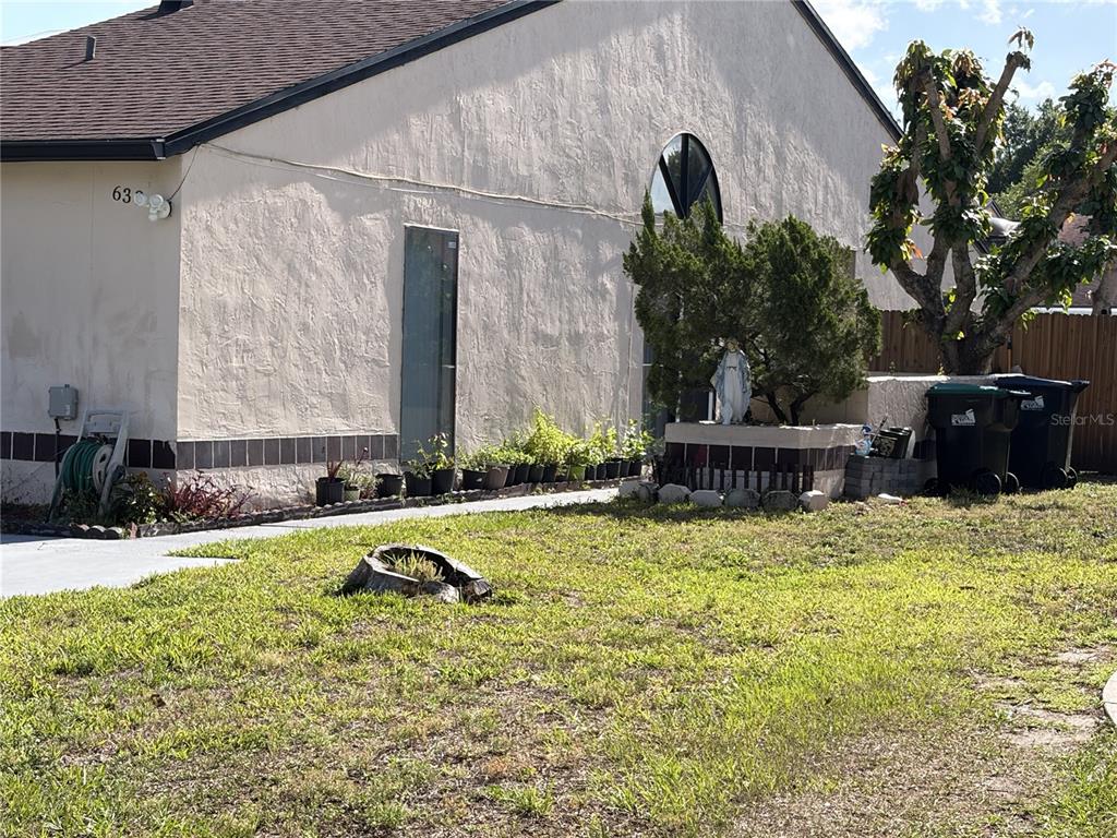 A beige stucco house exterior features a small statue, potted plants, and two trash cans — 639 GOLDEN SUNSHINE CIRCLE, ORLANDO, FL