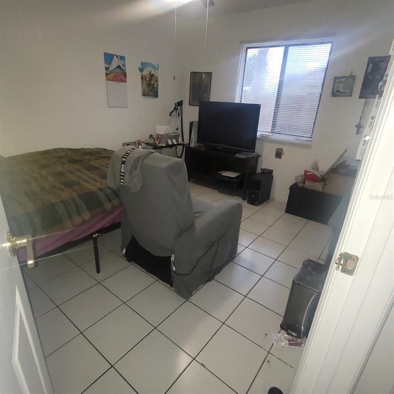 A bedroom features white walls, tile flooring, a bed, a recliner, and a television — 639 GOLDEN SUNSHINE CIRCLE, ORLANDO, FL