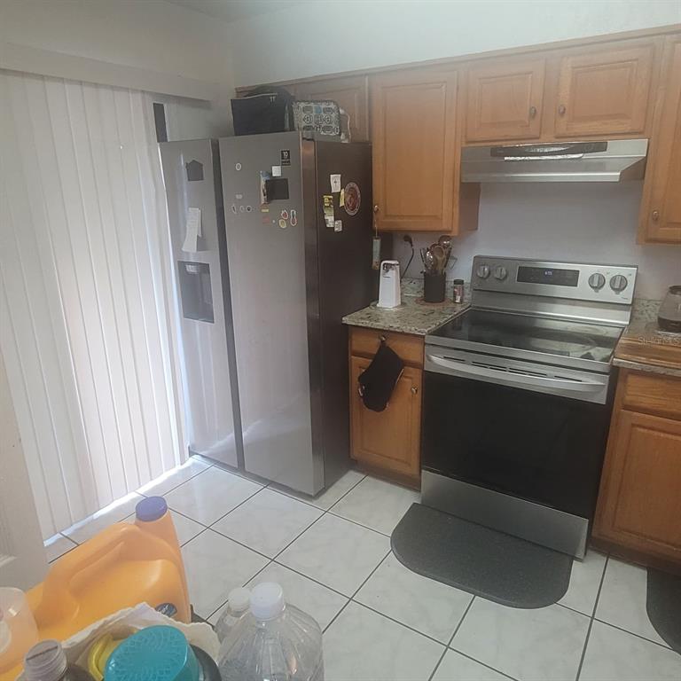 A kitchen features stainless steel appliances, wood cabinets, granite countertops, and white tile flooring — 639 GOLDEN SUNSHINE CIRCLE, ORLANDO, FL