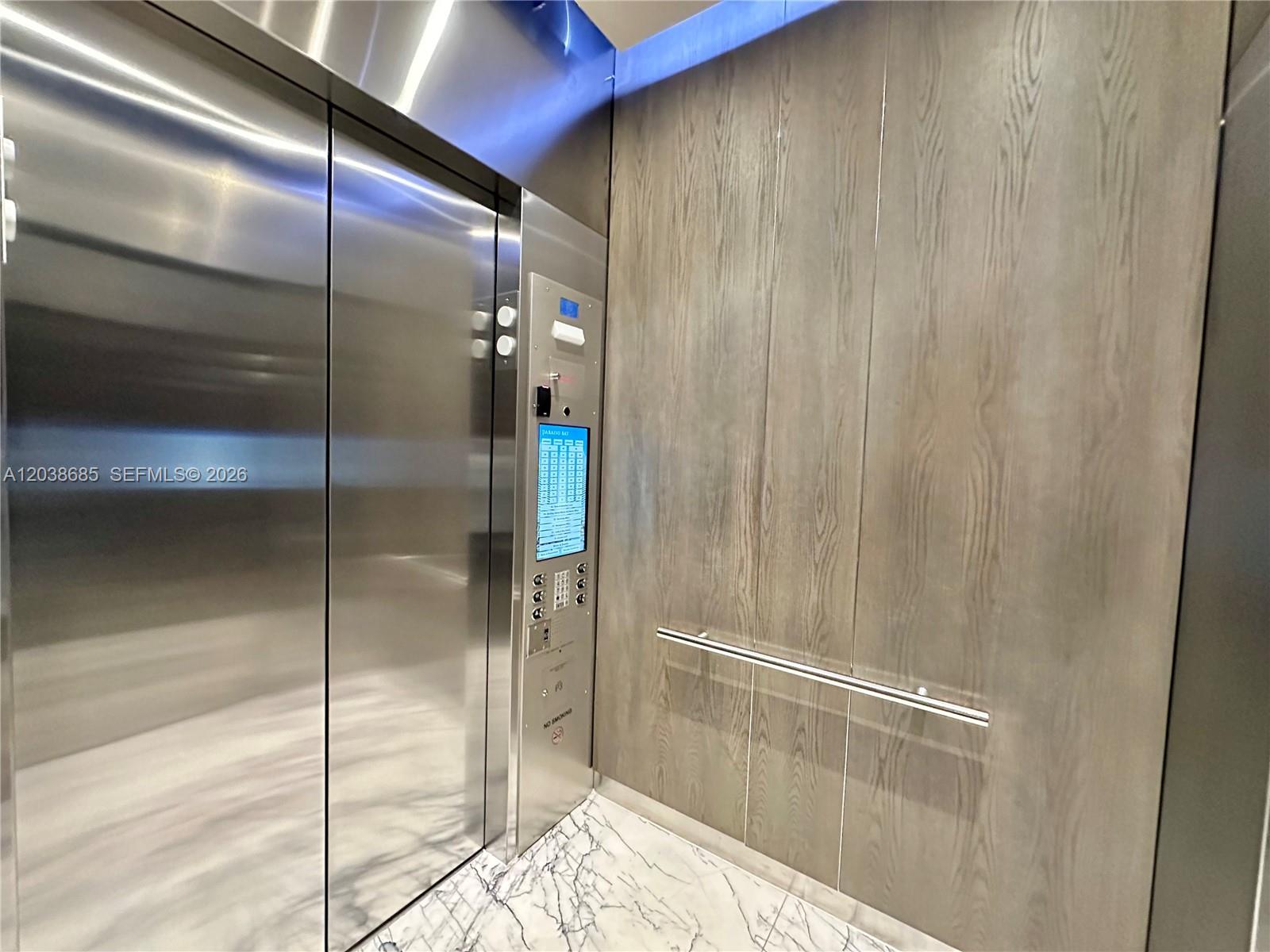 An elevator interior features stainless steel doors, wood paneling, and a marble floor — 650 NE 32nd St # 1404, Miami FL 33137, MIAMI, FL