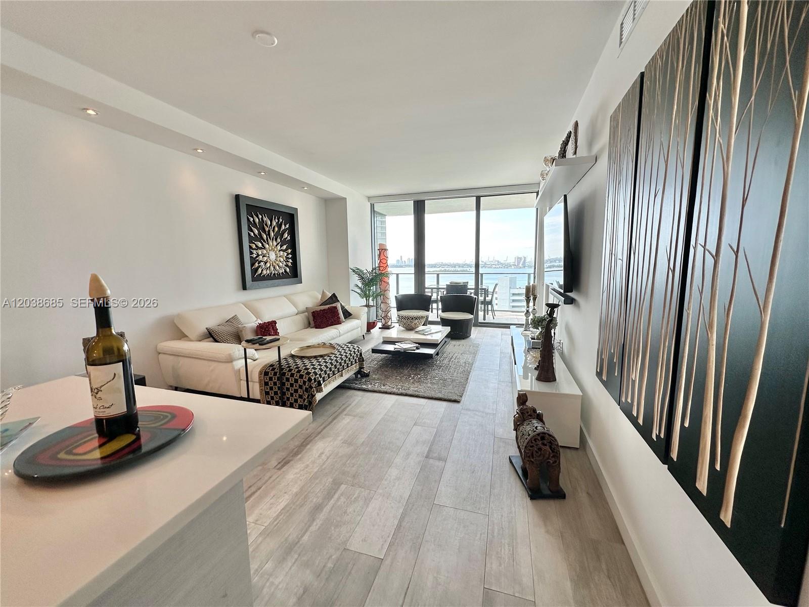 A modern living room features a white sofa, wood-look tile flooring, and a balcony view — 650 NE 32nd St # 1404, Miami FL 33137, MIAMI, FL