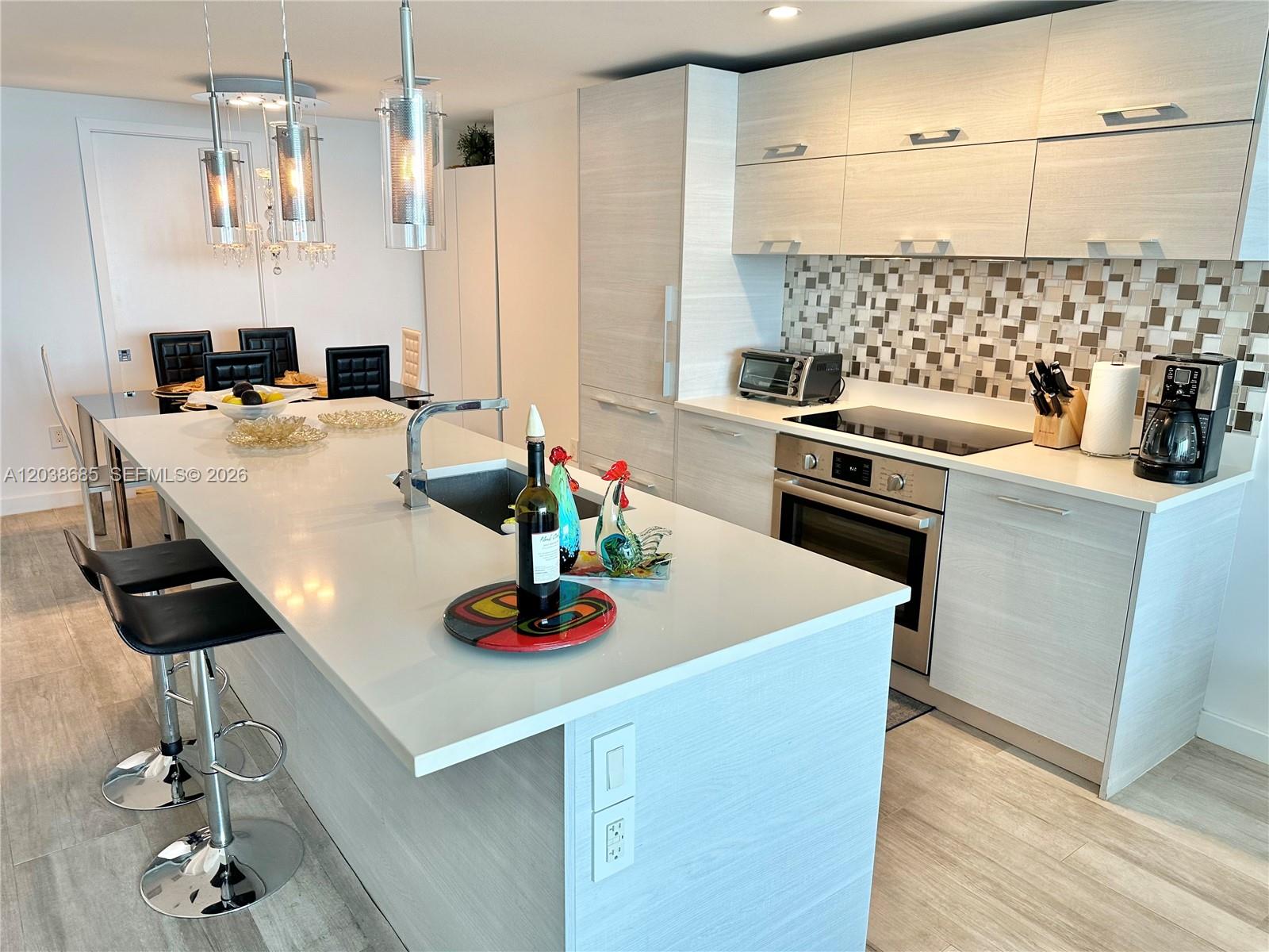 A modern kitchen features a white island, light wood cabinetry, and a mosaic tile backsplash — 650 NE 32nd St # 1404, Miami FL 33137, MIAMI, FL