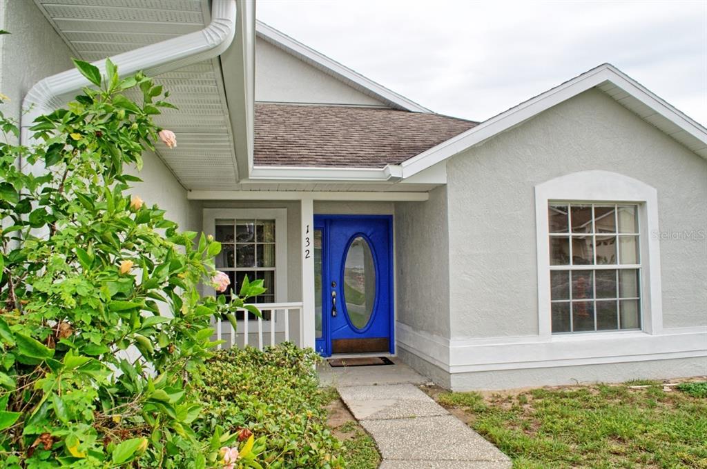 A light-colored house exterior features a bright blue front door and a concrete walkway — 132 AZALEA DRIVE, DAVENPORT, FL