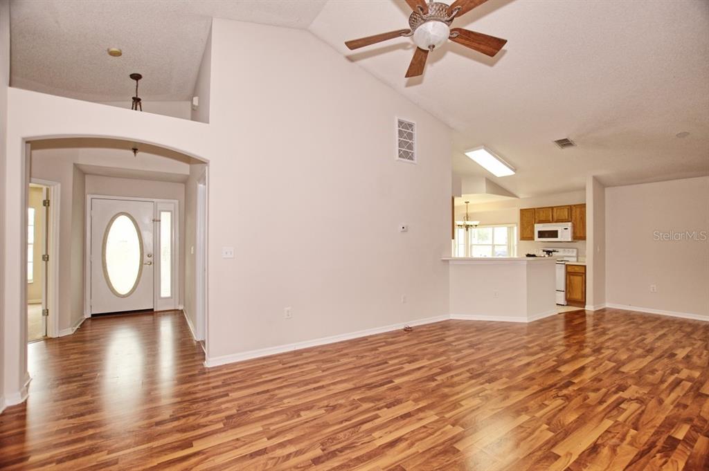 An open-concept living area with wood-look flooring, vaulted ceilings, and a view into the kitchen — 132 AZALEA DRIVE, DAVENPORT, FL