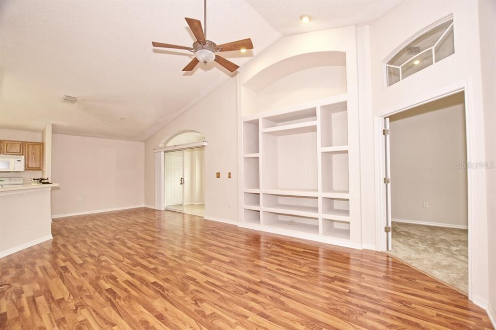 A living room with wood-look flooring, a vaulted ceiling, a ceiling fan, and built-in shelving — 132 AZALEA DRIVE, DAVENPORT, FL