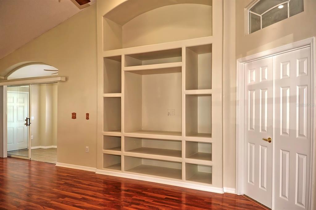 A living room features a large built-in shelving unit, hardwood floors, and white paneled doors — 132 AZALEA DRIVE, DAVENPORT, FL