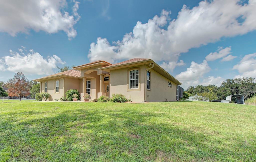 A single-story tan stucco house with a metal roof sits on a grassy lawn — 6930 69TH STREET E, PALMETTO, FL