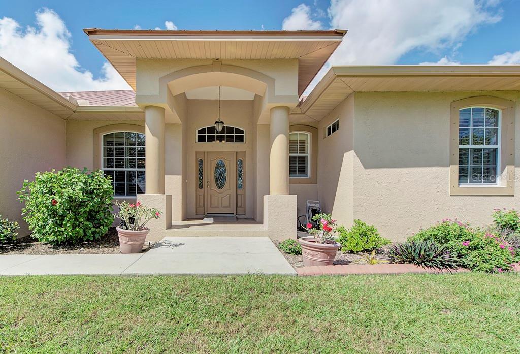 The exterior of a beige house features a covered entryway with two columns and a door — 6930 69TH STREET E, PALMETTO, FL