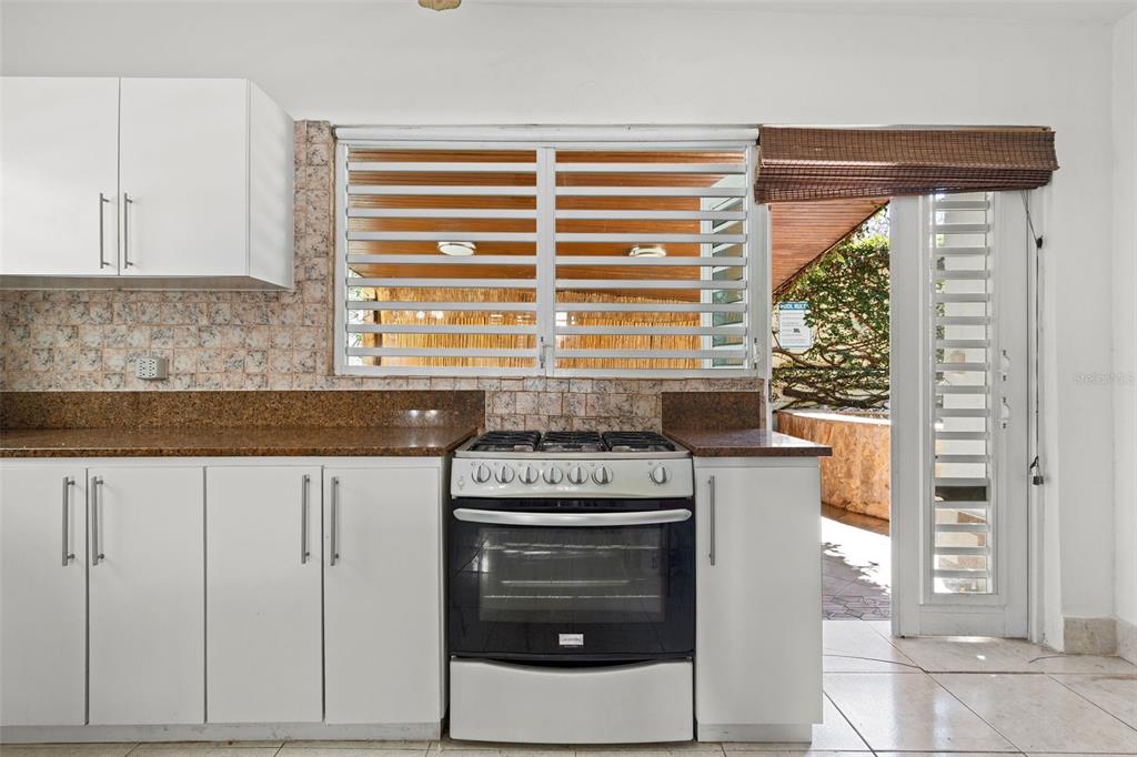 A kitchen features white cabinets, a gas stove, granite countertops, and a glass-paned exterior door — Ocean Park 2052 CACIQUE, SAN JUAN, PR