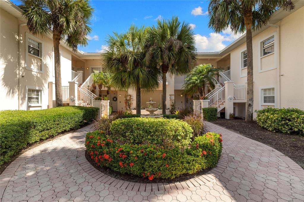 A paved courtyard features a central fountain, lush landscaping, and staircases leading to upper-level units — 4244 CENTRAL SARASOTA PARKWAY UNIT 716, SARASOTA, FL