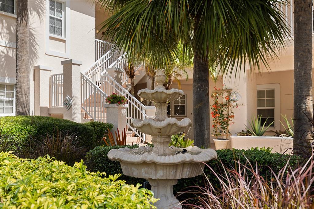 A three-tiered stone fountain sits in a courtyard in front of a multi-story building — 4244 CENTRAL SARASOTA PARKWAY UNIT 716, SARASOTA, FL