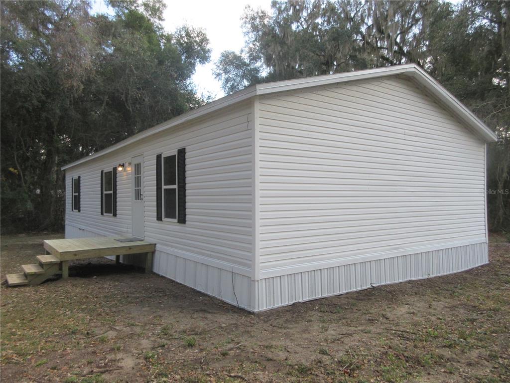 A white mobile home with light-colored siding and a wooden deck sits on a dirt lot — 2960 NE 159TH PLACE, CITRA, FL